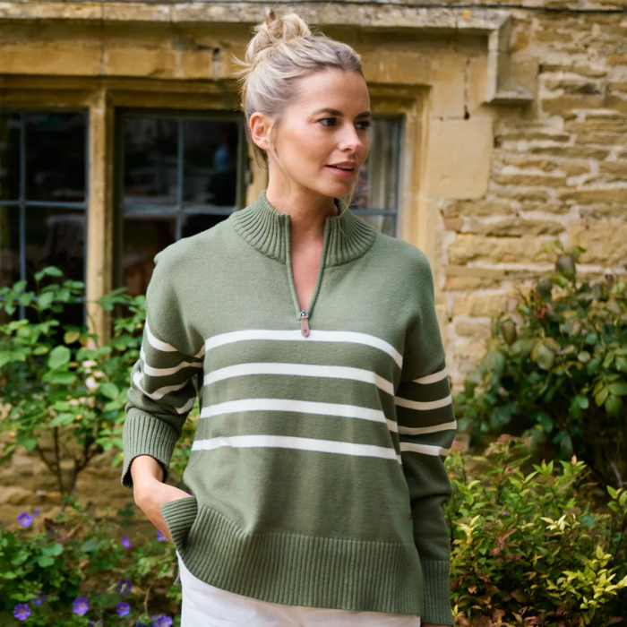 Woman wearing a green knitted top with white stripes standing in front of a cottage