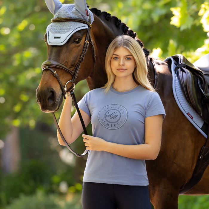 Woman wears a blue t-shirt standing by a horse in an outdoor setting