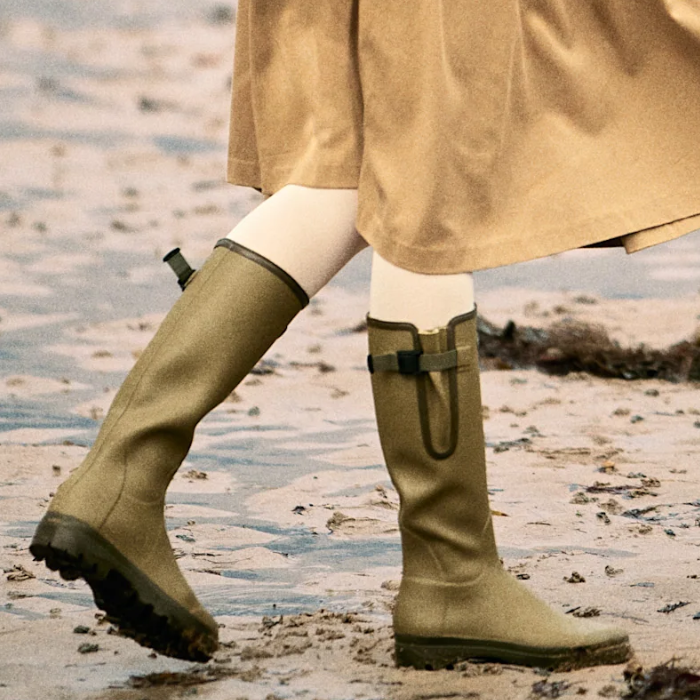 Person wears a pair of green wellington boots on a beach