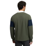 LeMieux AW26 Mens Rugby Shirt Varient LeMieux. A man viewed from the back wearing an olive green long-sleeve rugby shirt with navy blue color-blocked shoulder panels and a white collar, paired with dark jeans against a plain white background.