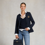Woman wearing a navy blazer with a logo, white shirt, and blue jeans, holding a black handbag on a light gray background. Holland Cooper Zoe Knit Jumper Navy