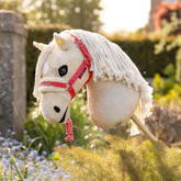 Plush toy horse with a pink bridle in a garden setting