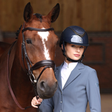 Lady wearing a navy riding hat, wearing a blue show jacket, holding a bay horse.
