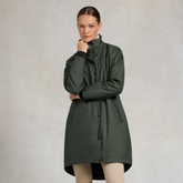 A woman modeling a dark olive green hooded raincoat against a textured light gray studio background.