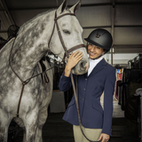 Woman in equestrian attire petting a gray horse in a stable.