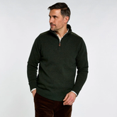 A man wearing a dark forest green quarter-zip knit sweater with a ribbed mock neck, cuffs, and hem, paired with brown corduroy trousers, photographed against a light gray studio background.