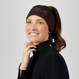 Pikeur AW26 Cotton Headband Variant Chocolate Brown. A woman wearing a dark brown knit cycling headband with 'PIKEUR' embroidered in light brown on the front, paired with a black ribbed turtleneck sweater, set against a solid light gray background.