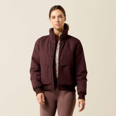 Lady wearimg a Brown/ Red coat against a beige background.