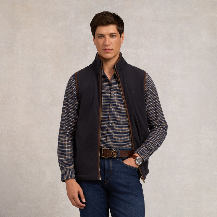 Holland Cooper Country Fleece Gilet (Men's) Variant Ink Navy. Man wearing navy gilet with brown detailing over a cheque shirt on a grey background.