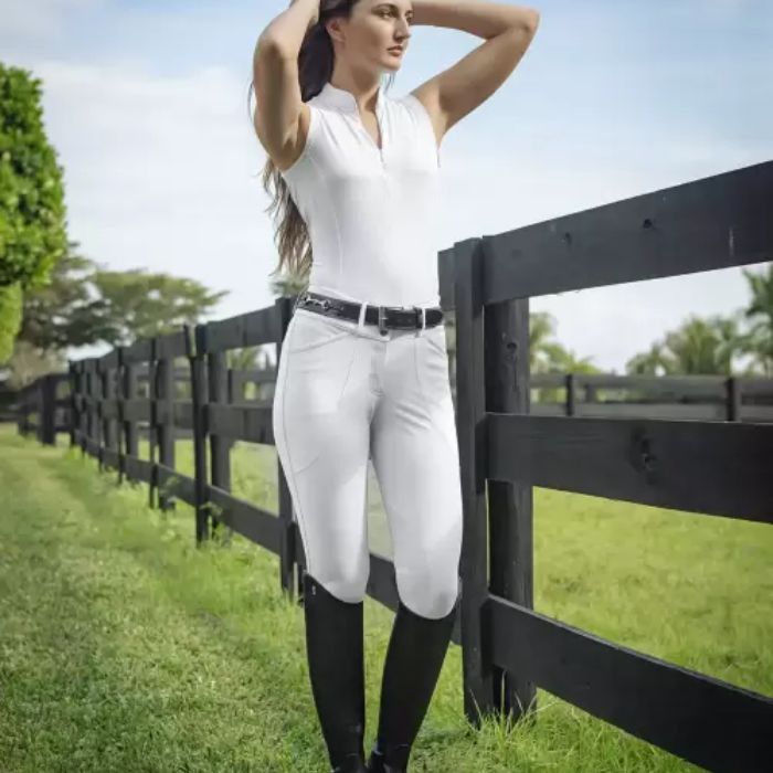 Woman in equestrian attire standing by a wooden fence in an outdoor setting