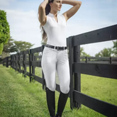 Woman in equestrian attire standing by a wooden fence in an outdoor setting