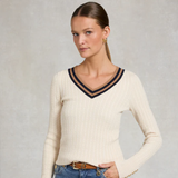 Woman wearing a cream sweater with navy trim against a plain background