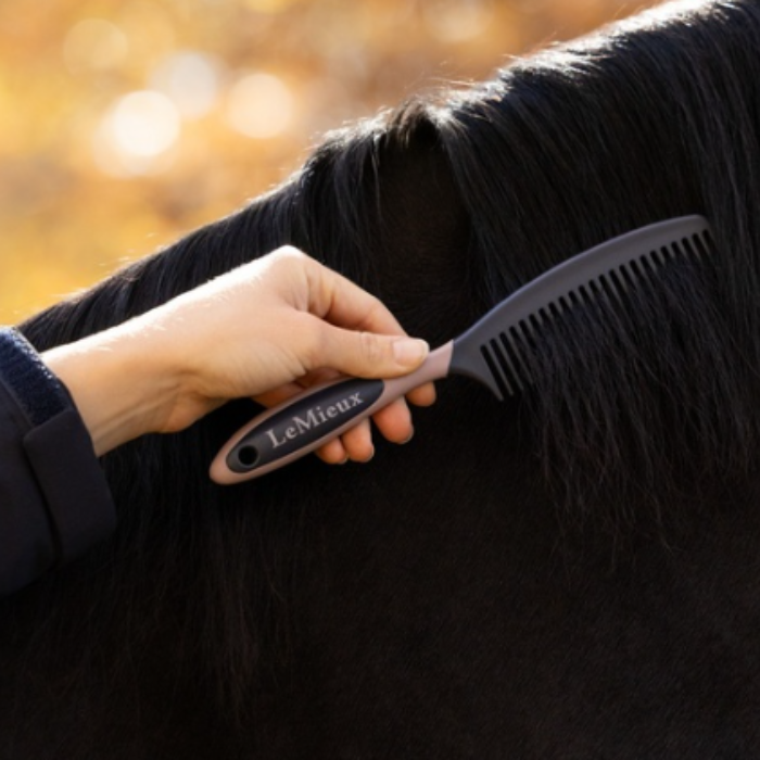 LeMieux AW26 Mane Comb Varient Navy. A hand holds a LeMieux horse grooming comb against a horse's dark black mane in an outdoor setting with a warm, blurred background.
