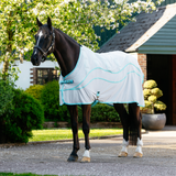 Horse wearing a white fly sheet with blue trim standing on a gravel path.
