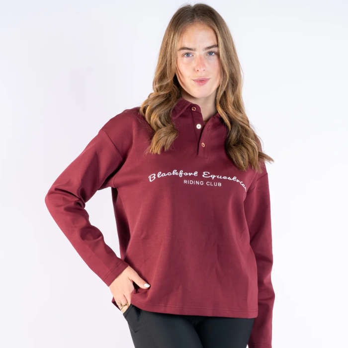 Blackfort Remi Rugby Shirt Variant Burgundy. Burgundy rugby shirt, with Blackfort Equestrian written accross the front against a greay background.