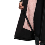 LeMieux AW26 Young Rider HydroShield Robe Varient Black. Close-up of a black outerwear garment with a soft pink sherpa lining, shown on a person whose hand and part of the body are visible against a plain white background.