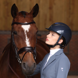 Lady wearing a navy riding hat, wearing a blue show jacket, looking at a bay horse.
