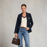 Woman wearing a navy blazer with a logo, holding a brown handbag, on a light gray background