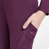 Close-up of a person wearing a fitted athletic legging in a deep plum purple, showing a side pocket with black rhinestone embellishments and a hand reaching into the pocket.