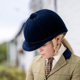 Person wearing a navy riding helmet and tweed jacket with a blurred outdoor background