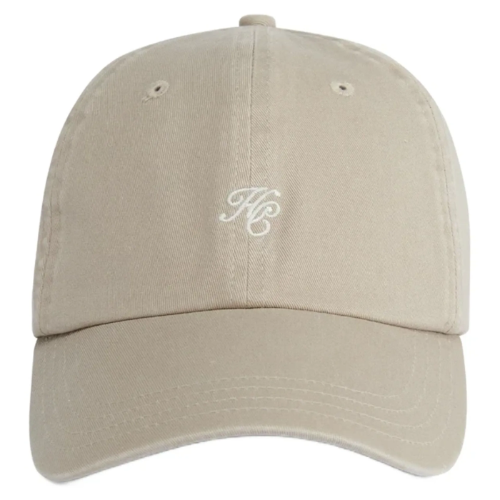 A beige baseball cap with a curved brim and an embroidered white monogram logo on the front, shown against a plain white background.