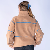 Blackfort AW26 Layla Fleece Variant Tan & Glacier. A person shown from the back wearing a tan sherpa fleece zip-up jacket with blue contrast stitching and a small embroidered logo on the upper back, against a light gray studio background.