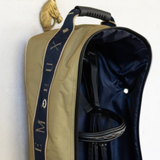 LeMieux AW26 Anatomical Bridle Bag Varient Gooseberry. A close-up of a tan equestrian bridle bag with a navy blue interior, a navy blue side strap featuring gold lettering, and a black handle, shown against a plain white wall.