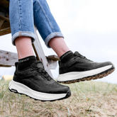 Person wearing navy sneakers with white soles on a beach.