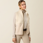 Ariat Yth Laviolette Full Zip Vest Varient Almond Milk. Lady wearing a cream fleece gilet with matching beige trousers on a light background.