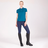 Person wearing a teal equestrian shirt, navy leggings, and black riding boots on a white background