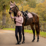 LeMieux AW26 Essence Close Contact Square Varient Wild Rose. Girl wearing a dusty pink jacket stood by a horse wearing a matching dusty pink set, stood in a driveway with a forest background.