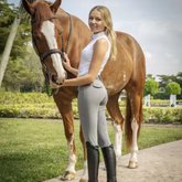 Woman in equestrian attire standing next to a brown horse in an outdoor setting