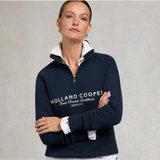 Holland Cooper Sporting Goods Zip Henley - Ink Navy. A woman modeling a navy blue quarter-zip sweatshirt with a white collar and white embroidered text reading 'HOLLAND COOPER Great British Excellence MMVIII' on the front, posed against a neutral gray background.