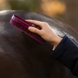 LeMieux AW26 Wizard Brush Trio Varient Wild Rose/Blackberry/ Willow. A close-up of a person's hand grooming a dark brown horse with a deep purple rubber bristle brush.