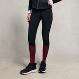 Holland Cooper Riding Sock Variant Oxblood Navy. A pair of model legs wearing leggins and burgundy knee length socks with navy trainers on grey background.