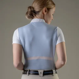 Woman wearing a light blue vest over a white shirt on a neutral background