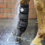 Horse leg with protective boot being rinsed under water, with a brick wall background