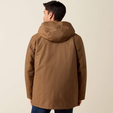 A man viewed from the back wearing a brown hooded jacket, paired with blue jeans, against a plain light beige studio background.