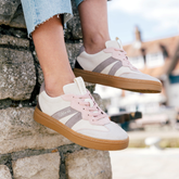 White and pink sneakers with brown soles worn by a person sitting on stone steps.
