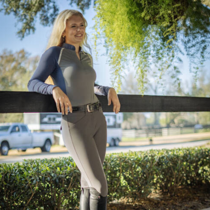 Person leaning on a fence wearing Navy and grey long sleeve top and grey leggings on faded background