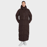Aztec Diamond Matte Long Puffer AW26 Variant Espresso. A model wearing a long, dark brown puffer coat with a front zipper and hood, paired with white sneakers, against a solid light gray background.