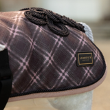LeMieux AW26 Toy Pony Heritage Rug Varient Cocoa. A close-up of a horse blanket with a brown and pink plaid pattern, featuring a black braided rope detail and a black leather brand patch that reads 'LEMIEUX HERITAGE'.