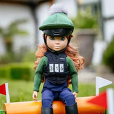 Doll in equestrian gear sitting on a barrel with blurred outdoor background
