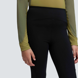 Close up of the waistband of a black pair of trousers with a green base layer tucked in against a grey background.