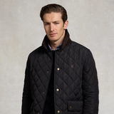 A man wearing a navy diamond-quilted jacket with a dark brown ribbed collar, gold-tone snap buttons, and a small embroidered logo on the chest, set against a textured light gray background.