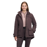 LeMieux AW26 Heritage Beatrice Waterproof Coat Variant Cocoa. A woman modeling a dark brown hooded jacket with a quarter-zip front, button snap details, and large front flap pockets, paired with matching brown pants and a light pink top, against a solid white background.