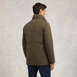 Holland Cooper Stamford Field Coat (Men's) Variant khaki. A man wearing an olive green puffer jacket, shown from the back, standing against a textured light gray background.