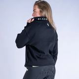 Person wearing a black sweater with partially visible branding on the back, standing against a light grey background.