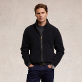 Holland Cooper Country Fleece Jacket (Men's) Variant Black. Man wearing a long sleeve black fleece with black leather trim detailing and a small HC logo on a beige background.