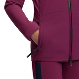 LeMieux AW26 Young Rider Betty Lightweight Jacket Varient Blackberry. Close-up of a person wearing a fitted athletic jacket in a deep berry-purple color, with a hand in a side pocket and a dark navy side panel on the matching pants against a white background.